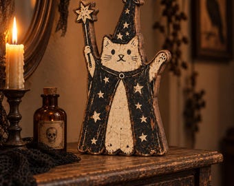 Pode incluir: Um recorte de madeira de um gato vestido de mago, com uma túnica preta e um chapéu pontudo decorados com estrelas brancas. O gato segura uma varinha com ponta de estrela numa pata e tem um rosto cor de creme com bigodes pretos.