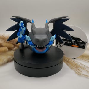 Könnte beinhalten: Grau-blaue Drachenfigur mit dunkelblauen Flügeln und blauen Flammen. Die Figur steht auf einem schwarzen, kreisförmigen Sockel. Der Drache hat einen blauen Mund und blaue Akzente auf Hörnern und Flügeln. Weißes kreisförmiges Logo mit dem Text "PRINTOSAURUS".