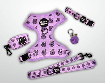 May include: A lavender pet harness, leash, collar, waste bag dispenser, and keychain set featuring a repeating dark purple fruit pattern. Each item includes a black Cosmic Canine logo patch. The set includes black plastic buckles and metal hardware.