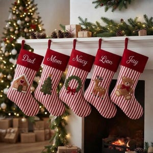 Puede incluir: Cinco calcetines navideños con rayas verticales rojas y blancas y un puño rojo sólido. Cada puño tiene nombres bordados en blanco: Dad, Mom, Nacy, Lion y Jay. Los calcetines muestran apliques de una casa de jengibre, árbol, corona, ciervo y oso.