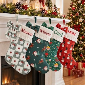 Puede incluir: Cuatro calcetines navideños personalizados colgados en fila. El primero es de cuadros blancos y grises con gnomos y el nombre Mason. El segundo es verde oscuro con renos y gnomos y el nombre Wiliam. El tercero es verde con adornos y el nombre Dad. El cuarto es rojo con muñecos de nieve y el nombre MOM.