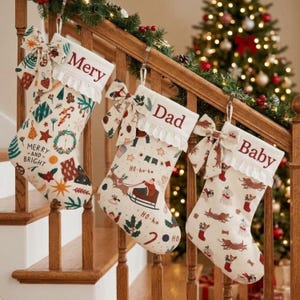 Puede incluir: Tres calcetines navideños de color crema colgados en una barandilla de escalera de madera. Cada calcetín presenta un borde de encaje blanco, un lazo de tela y un estampado festivo único. Los nombres Mery, Dad y Baby están bordados.