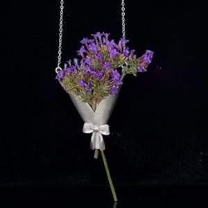 May include: A silver-toned necklace pendant shaped like a bouquet of purple flowers. The flowers are contained in a cone-shaped holder with a bow at the base. The pendant hangs from a delicate chain.
