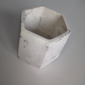 Può includere: Un vaso esagonale bianco con un motivo marmorizzato. Il piccolo contenitore aperto ha una superficie strutturata con venature grigie. Il vaso è adatto a piccole piante o piante grasse.