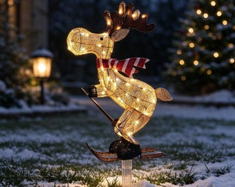 May include: A light-up outdoor reindeer decoration made of gold-toned wire mesh, wearing a red and white striped scarf. The reindeer is depicted in a skiing pose, mounted on a clear plastic stake, and illuminated by internal warm white LED lights.