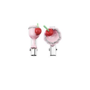 May include: A pair of pink hair clips, one resembling a cocktail glass and the other a seashell, each decorated with a red cherry and rhinestones. The clips have silver metal clasps, offering a fun and fashionable hair accessory.