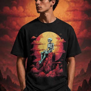 May include: Black t-shirt with a graphic of a skeleton seated on a red rock formation, set against a yellow and red sunset. The t-shirt has a crew neck design.