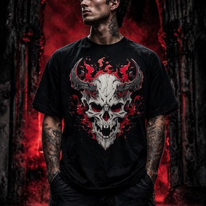 May include: Black t-shirt featuring a detailed skull design with horns and flames in red and gray. The graphic is centered on the shirt. The person is wearing black pants and has tattoos on their arms and neck.