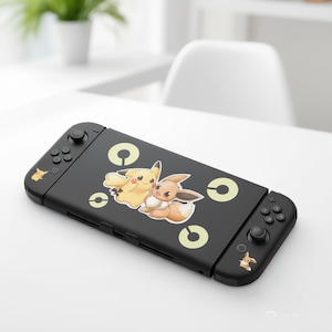 May include: Black Nintendo Switch console with a Pikachu and Eevee design. The console features yellow and brown cartoon characters, with yellow circle accents. The controllers have small Pikachu graphics.
