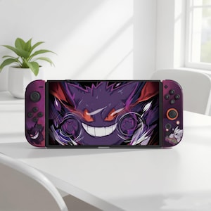 May include: A Nintendo Switch console with a custom design featuring a purple Gengar character. The Joy-Con controllers are purple with black buttons and a Gengar silhouette. The screen displays a detailed Gengar graphic.