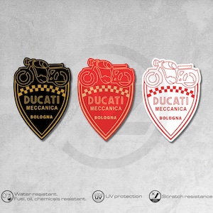 May include: Three motorcycle-themed decals in black and gold, red and gold, and red and white. Each features a motorcycle silhouette above the text "DUCATI MECCANICA BOLOGNA" within a shield shape. The decals are water, fuel, oil, and chemical resistant, with UV protection and scratch resistance.