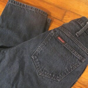 May include: A pair of dark blue denim jeans with a back pocket that has the word "GIBSON" stitched in red.