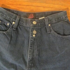 May include: A pair of dark blue denim jeans with a button fly and a single back pocket. The jeans have a brand label on the back waistband.