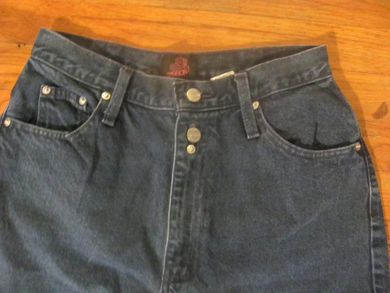 May include: A pair of dark blue denim jeans with a button fly and a single back pocket. The jeans have a brand label on the back waistband.