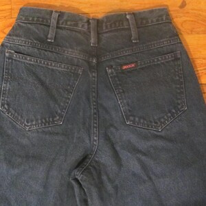 May include: A pair of dark blue denim jeans with a back pocket that has the word "GRACIOUS" stitched on it.