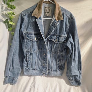 May include: Light blue denim jacket with a brown corduroy collar. The jacket has silver buttons, two chest pockets, and two side pockets. The label reads "Banana Republic".