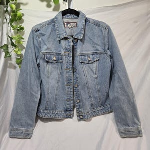 May include: Light blue denim jacket with silver buttons and two chest pockets. The jacket has a classic collar and a button-up front. The Old Navy label is visible on the back of the collar. A casual outerwear piece.
