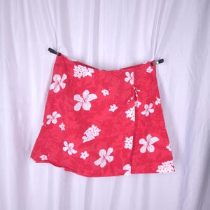 May include: A red wrap skirt with a white floral print. The skirt has a tie at the waist and a slit on the side.