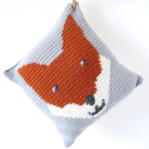 May include: A gray crocheted pillow with a fox face design in orange, white, and gray.