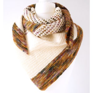 May include: A crocheted shawl with a white and multi-colored design. The shawl is folded and draped over a white mannequin.