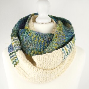 May include: A white crocheted infinity scarf with a green, blue, and yellow patterned section.