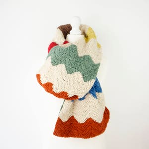 May include: A crocheted scarf with a chevron pattern in shades of beige, green, blue, red, and orange.