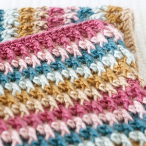 Puede incluir: Primer plano de una manta de ganchillo multicolor con rayas de color rosa, beige, azul claro y azul oscuro.