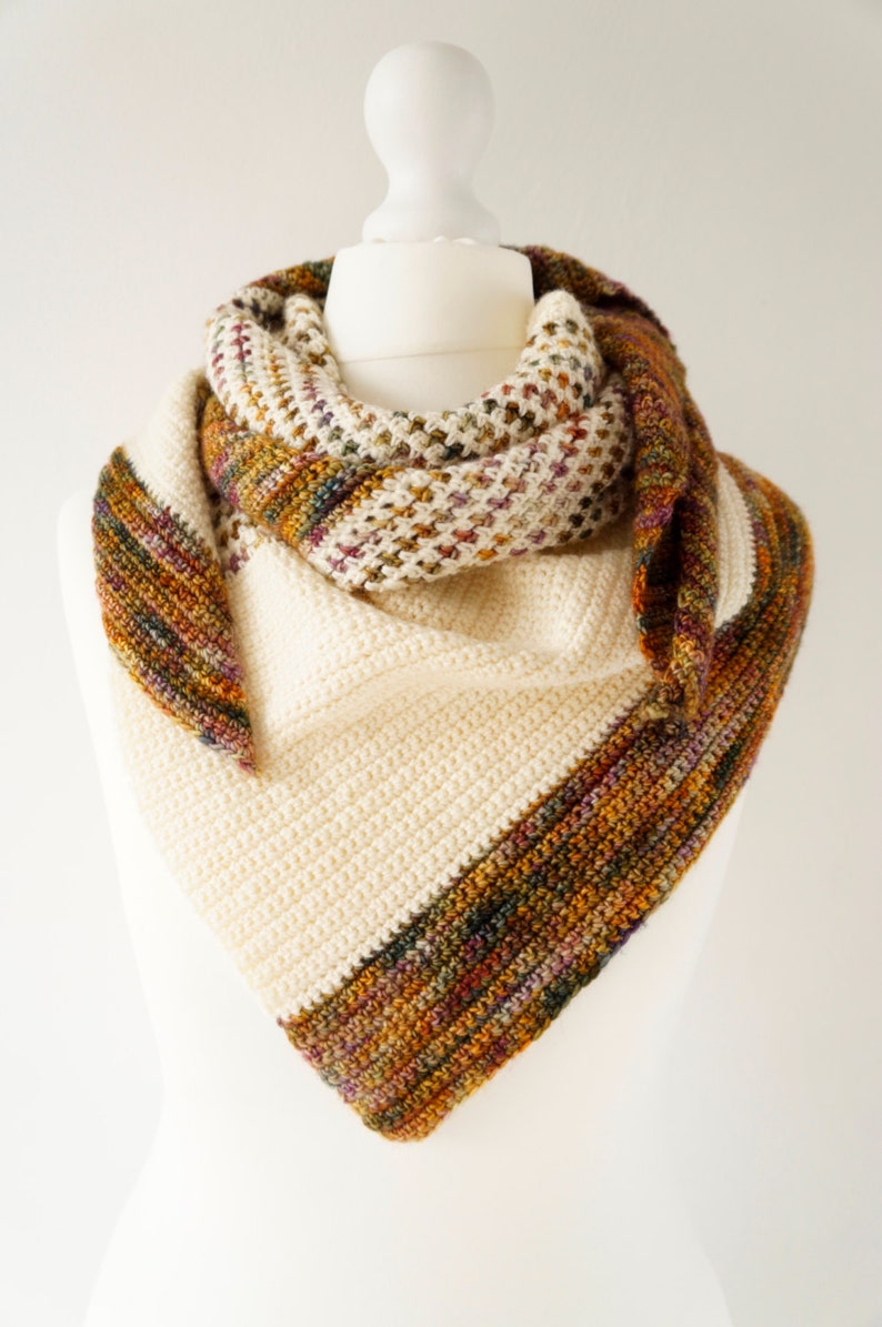 May include: A triangular crocheted shawl with a cream coloured base and a multi-coloured border. The border features shades of brown, orange, green, and purple.