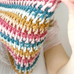 Puede incluir: Una bufanda de ganchillo colorida con rayas de hilo rosa, azul, blanco y marr&oacute;n.