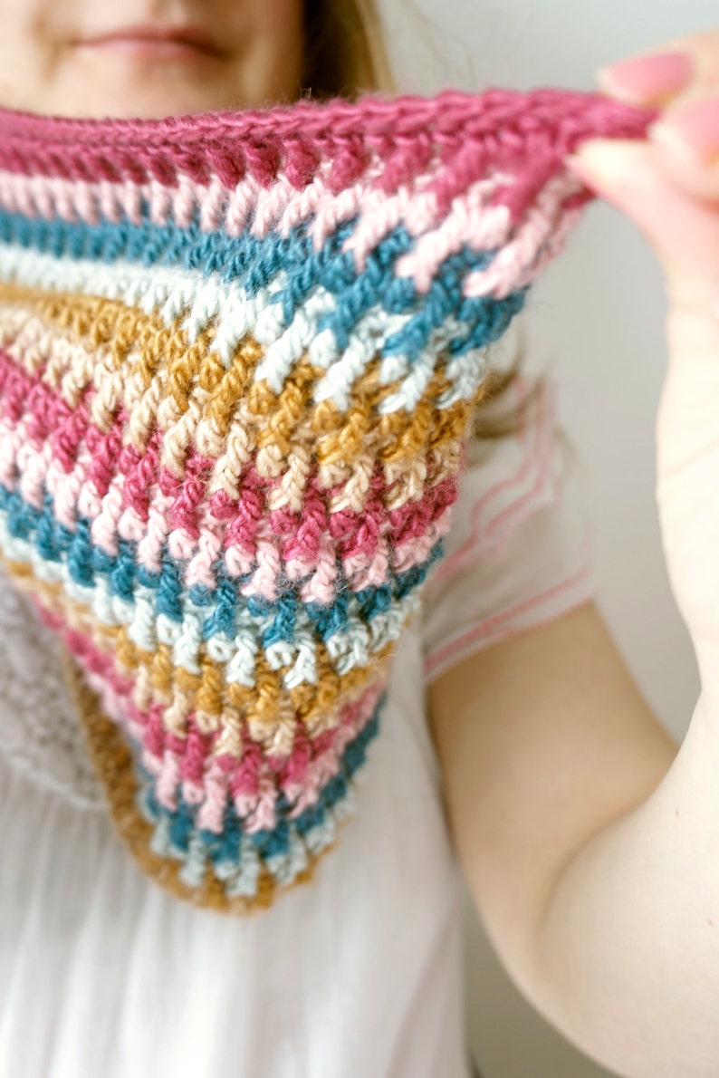 Puede incluir: Una bufanda de ganchillo colorida con rayas de hilo rosa, azul, blanco y marr&oacute;n.