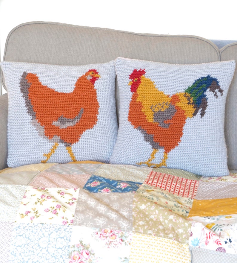 May include: Two crocheted throw pillows with a rooster and hen design. The pillows are on a couch with a patchwork quilt.