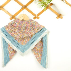 May include: A handmade crochet shawl in a triangular shape, featuring a hood. The shawl has a multicolored pattern with pink, yellow, and blue hues. The edges are trimmed with a light blue border and a white accent.
