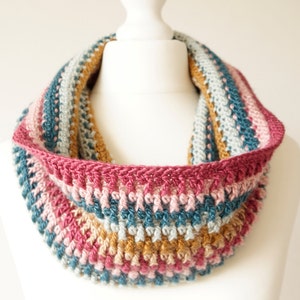 Puede incluir: Una capucha de ganchillo con un patr&oacute;n de rayas multicolores en tonos de rosa, azul y marr&oacute;n. La capucha est&aacute; hecha con un punto texturizado y tiene un dise&ntilde;o simple y elegante.