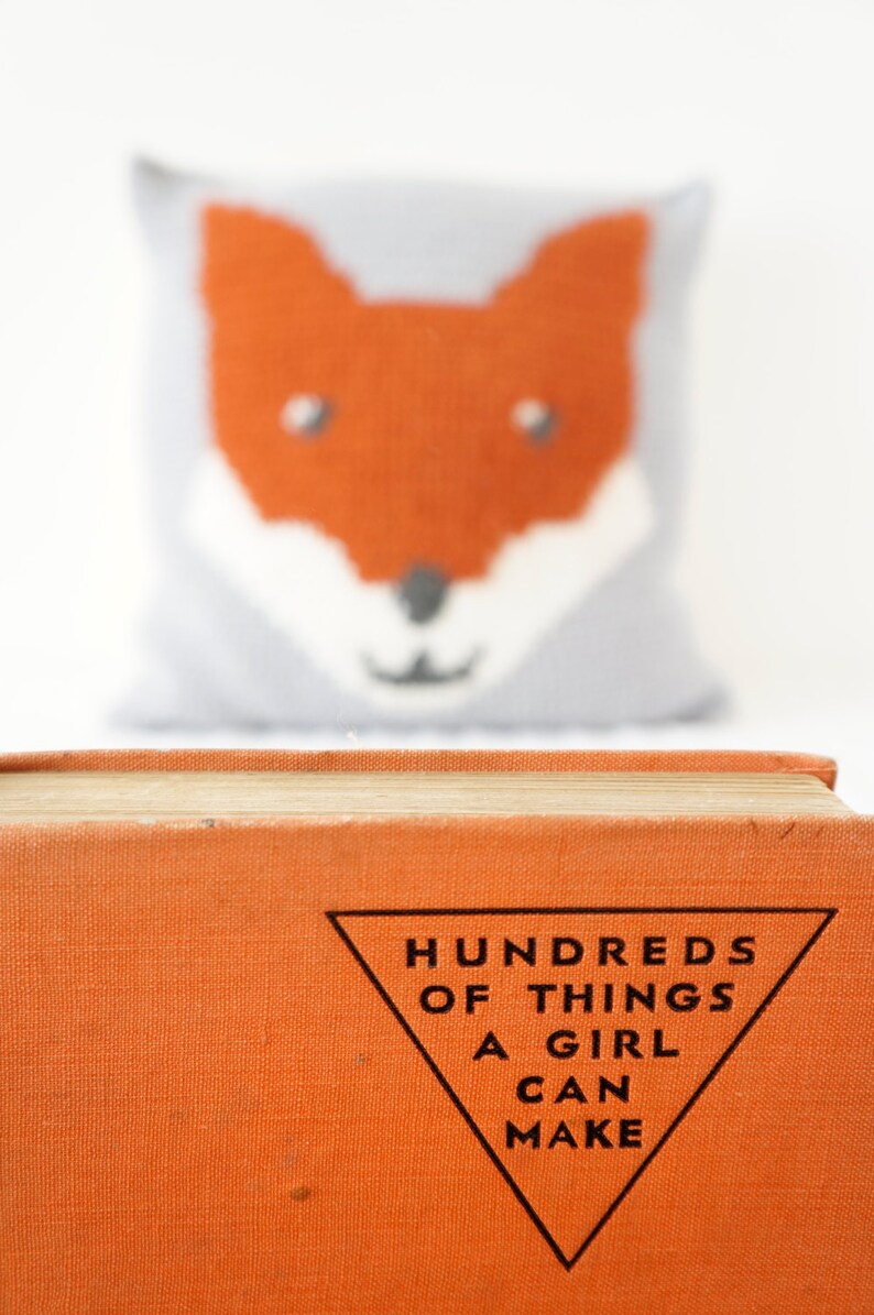 May include: An orange book with the title "Hundreds of Things a Girl Can Make" printed in black on a white triangle.