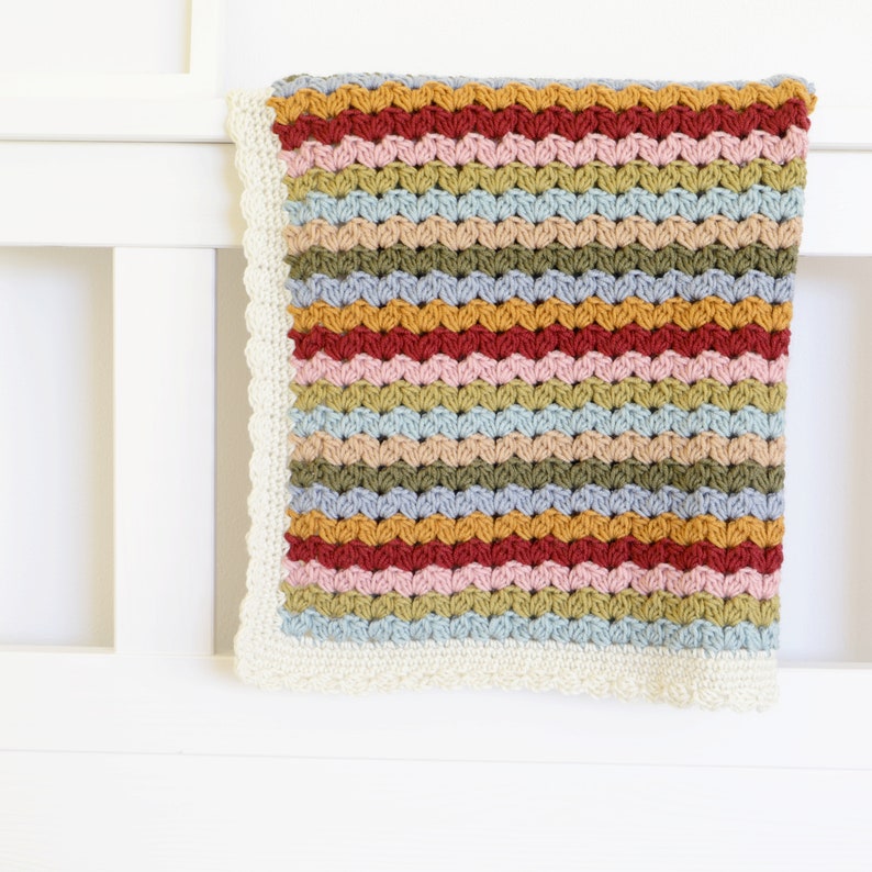 May include: A multi-colored striped crochet baby blanket with a white crocheted border.