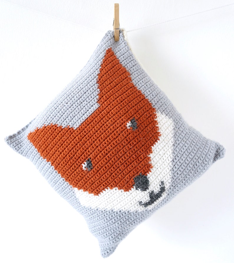 May include: A gray crocheted pillow with a fox face design in orange, white, and gray.