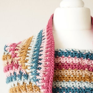 Puede incluir: Un cuello de punto de ganchillo con un patr&oacute;n de rayas en tonos de rosa, azul verdoso, beige y marr&oacute;n. El cuello se muestra en un maniqu&iacute; blanco.
