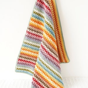 May include: A colorful striped crochet baby blanket with a textured stitch pattern. The blanket is hanging from a wooden clothespin.