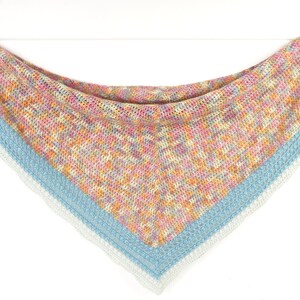 May include: A handmade, colorful shawl in a triangular shape, suspended from a clothesline. The shawl features a mix of pastel colors, including pink, orange, and blue, with a light blue border and white trim.