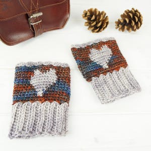 May include: A pair of gray knitted wrist warmers with a white heart design. The wrist warmers have a multi-colored pattern of blue, orange, and brown.