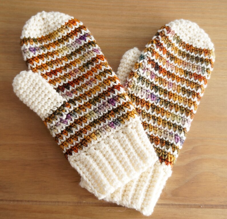 May include: A pair of crocheted mittens with a striped pattern in shades of brown, orange, and white.