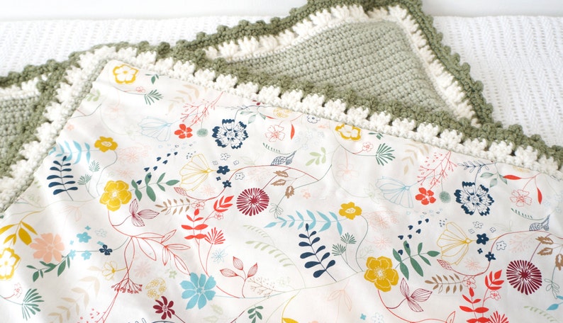 Puede incluir: Una manta de beb&eacute; de crochet verde con un borde de crochet blanco. La manta tiene un estampado floral sobre un fondo blanco.