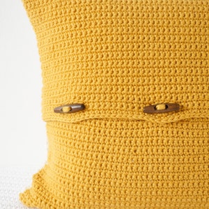 May include: A mustard yellow crocheted pillow with wooden button closures.