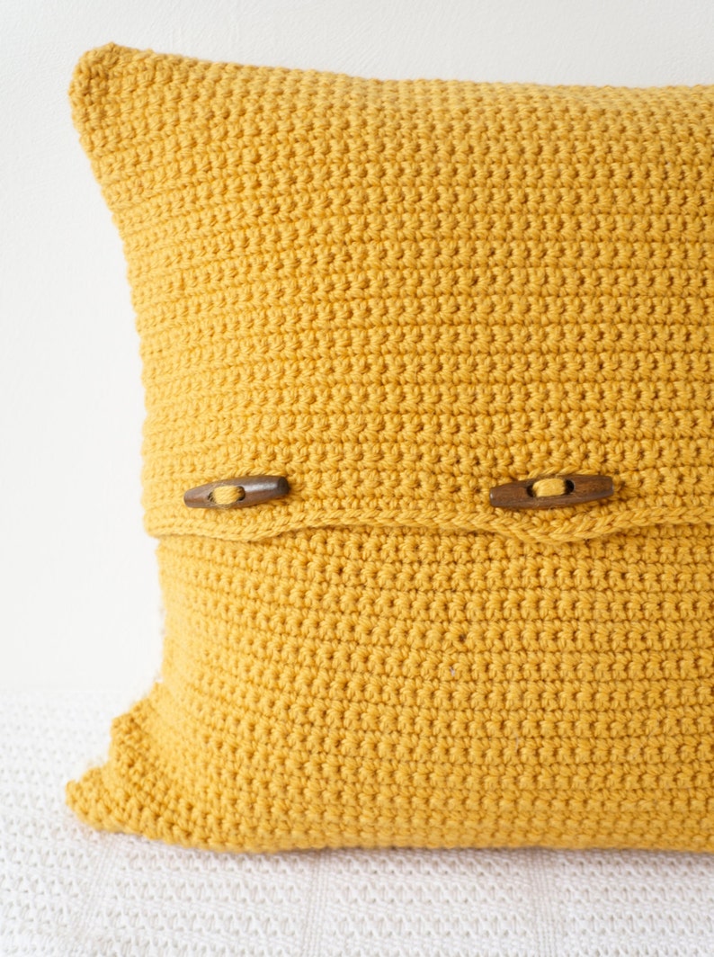 May include: A mustard yellow crocheted pillow with wooden button closures.