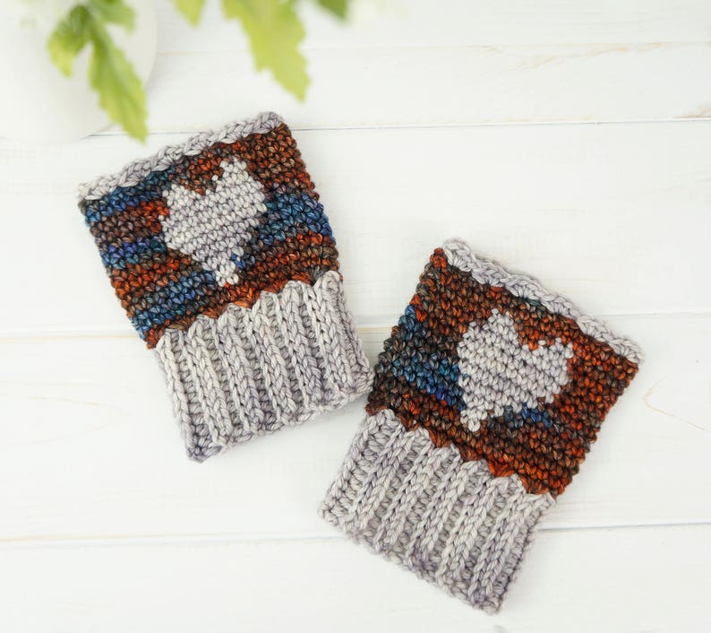 May include: A pair of gray and brown crocheted wrist warmers with a white heart design.