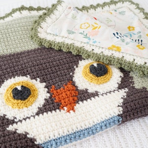 Puede incluir: Una manta de beb&eacute; de ganchillo con un dise&ntilde;o de b&uacute;ho verde y marr&oacute;n. La manta tiene un forro de tela blanca con flores y un borde de ganchillo verde.