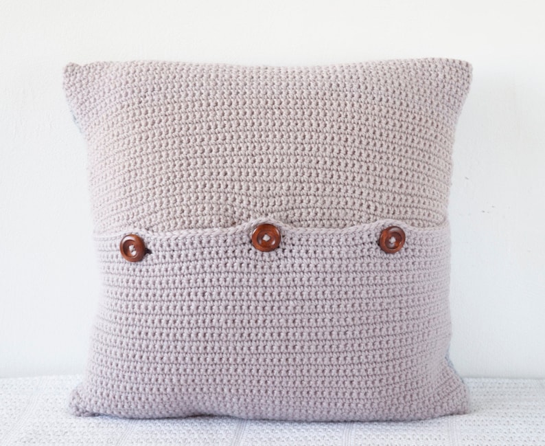 May include: A light pink crocheted pillow with a pocket and three wooden buttons.
