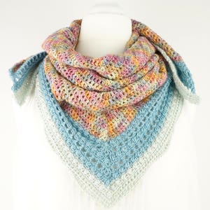 May include: A colorful, handmade crochet shawl displayed on a mannequin. The shawl features a mix of pastel colors, including pink, yellow, blue, and gray. The triangular design is visible, with a textured stitch pattern.