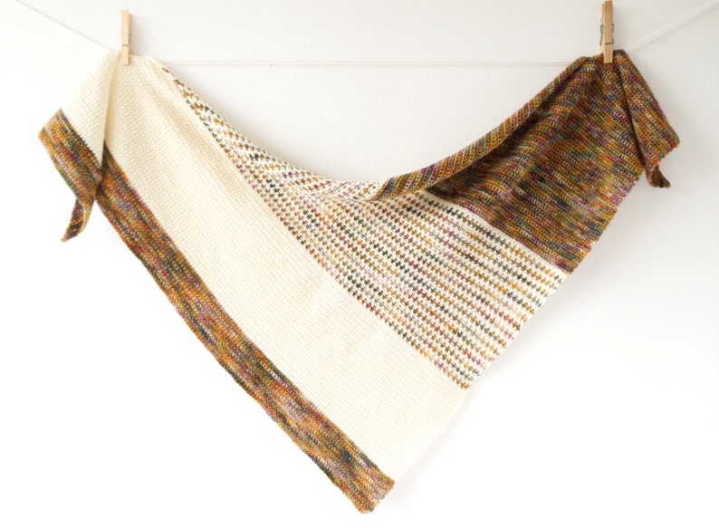 May include: A triangular shawl with a white centre and a brown, multi-coloured border. The shawl is crocheted and has a fringed edge.