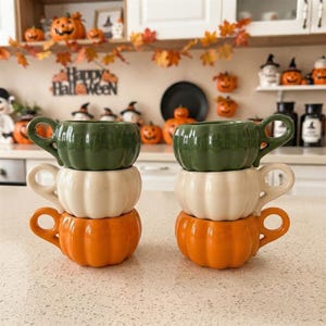 Könnte beinhalten: Zwei Stapel aus je drei kürbisförmigen Keramiktassen. Jeder Stapel besteht aus einer grünen Tasse oben, einer cremefarbenen Tasse in der Mitte und einer orangefarbenen Tasse unten. Die Tassen haben gerippte Seiten und einen seitlichen Henkel.
